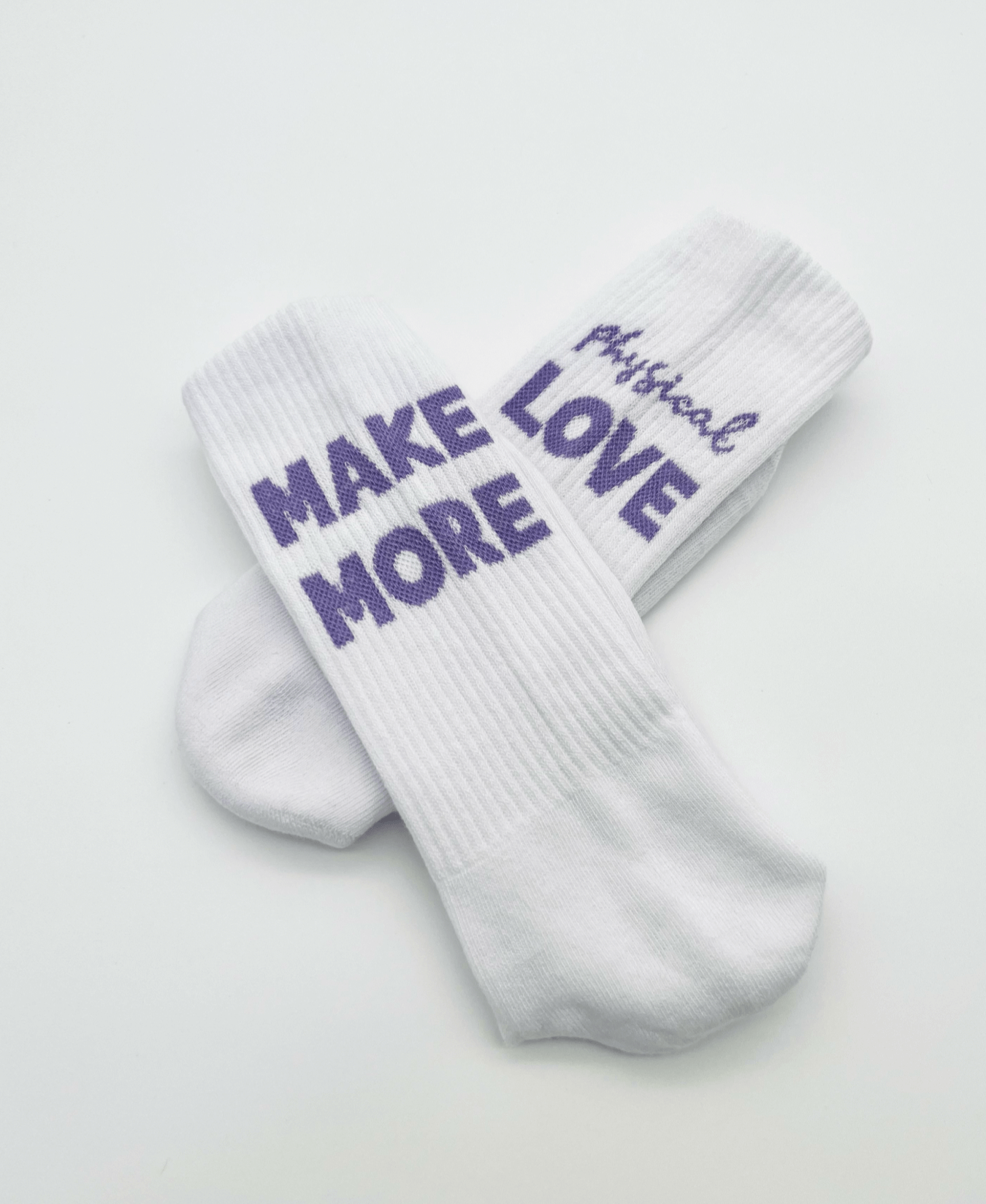 Weiße Tennissocken aus der MMPL Serie mit eingewebter Aussage in lila: Linke Socke: "Make More" und rechte Socke: "physical love"